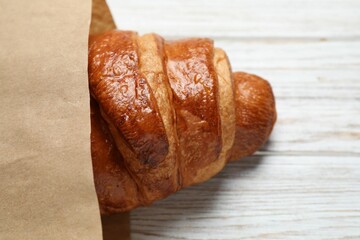 Paper bag with fresh croissant on wooden table, top view