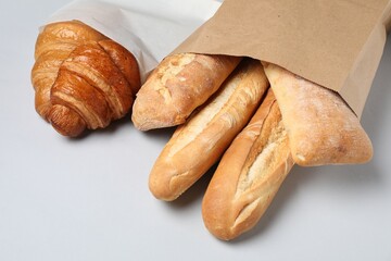 Paper bags with fresh pastries on white background, closeup