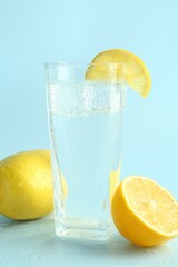 Soda water with ice cubes in glass and fresh lemons on light blue background
