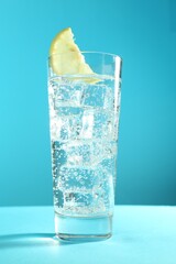 Soda water with lemon and ice cubes in glass on light blue background