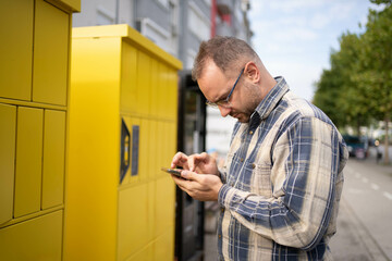 Man interacts with his smartphone near a bright yellow locker on a sunny day