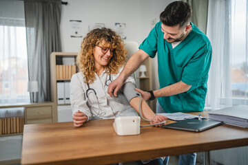 Fototapeta premium man doctor measure blood pressure to his colleague female doctor