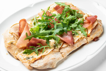 A delicious flatbread topped with prosciutto and fresh arugula, beautifully presented on a white plate. Perfect for gourmet food promotions and culinary articles.