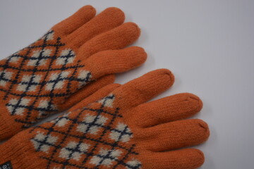 Warm, soft, winter items and household items. Beautiful orange, gray, insulated, knitted gloves are located on a white plastic background.