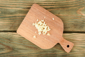 Top view of chopped garlic on wooden cutting board.