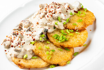 A plate of crispy golden pancakes topped with a creamy mushroom sauce and garnished with fresh green onions, perfect for a delicious savory meal or brunch.