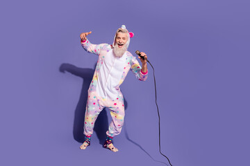 Joyful young man in trendy unicorn pajama singing joyfully against a vibrant purple background