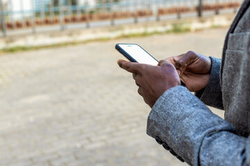 Portrait of an elegant and handsome black businessman using a smartphone in front of a m odern building in a city