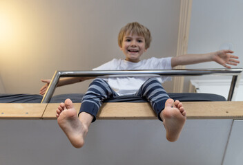 joyful boy stretches while sitting on a high bed after waking up. In the foreground, the child's bare feet are in focus. Wake up early in the morning easily and fun © Anna