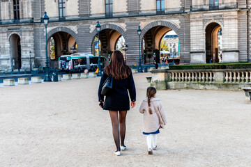 A woman and a little girl are leisurely walking in front of a building. Paris, France