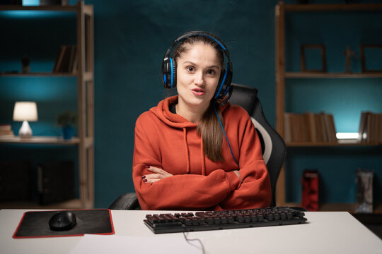 E-sport female gamer play video game at home using pc. Brunette woman gaming player looking camera with crossed arms, broadcast live streaming online.