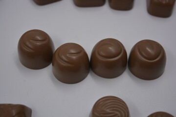 Food, food, very tasty milk candies are located on white plastic. Chocolates are made in the form of leaves, walnuts, medallions, round and square shapes.