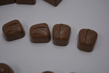 Food, food, very tasty milk candies are located on white plastic. Chocolates are made in the form of leaves, walnuts, medallions, round and square shapes.
