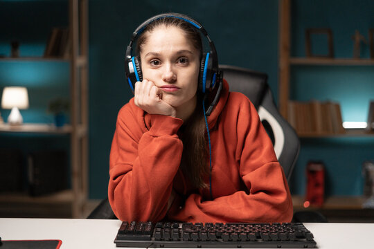 E-sport female gamer play video game at home using pc. Brunette woman gaming player looking to camera thoughtfully, broadcast live streaming online in the living room - Powered by Adobe