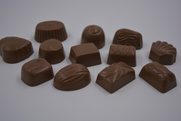 Food, food, very tasty milk candies are located on white plastic. Chocolates are made in the form of leaves, walnuts, medallions, round and square shapes.