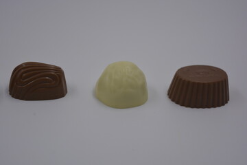 Food, food, very tasty milk candies are located on white plastic. Chocolates are made in the form of leaves, walnuts, medallions, round and square shapes.