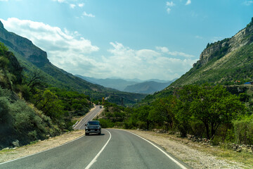 A car is driving down a road in a mountainous area