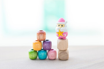 Christmas card background idea, colourful wooden beads stack with pink Santa Clause and star on wooden cube over blurred background, outdoor day light