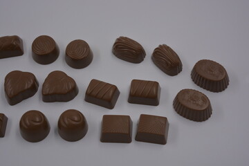 Food, food, very tasty milk candies are located on white plastic. Chocolates are made in the form of leaves, walnuts, medallions, round and square shapes.