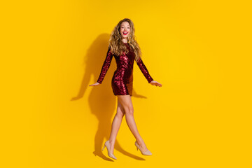 Glamorous young woman in red sequin dress posing against vibrant yellow background with confident and joyful expression