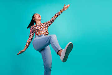 Photo of attractive young woman excited dancing step look empty space dressed stylish colorful clothes isolated on cyan color background
