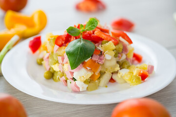 vegetable salad of boiled vegetables, with peas, sausage, sweet pepper. On a wooden table