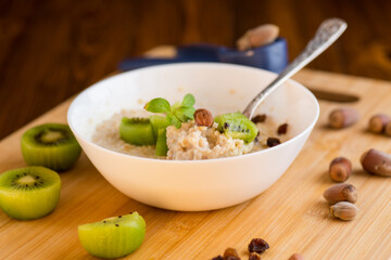 cooked oatmeal with kiwi, honey and nuts in a bowl on a wooden table