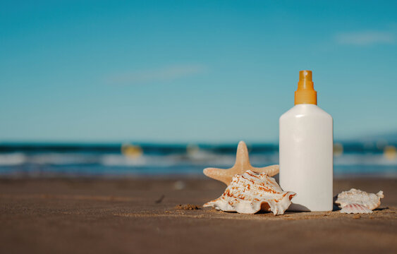 Sunscreen bottle on sandy beach with seashells and starfish under clear blue sky