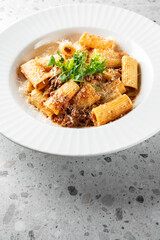 A delicious serving of rigatoni pasta topped with rich meat sauce, garnished with fresh herbs, served in a white bowl on a marble surface, perfect for food lovers and culinary enthusiasts.
