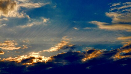 Fototapeta premium Blue sky, white, yellow and orange different types of clouds illuminated during sunset on windy weather - abstract background with natural pattern of clouds. Topics: air space, atmosphere, meteorology