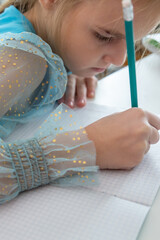 Little school girl sit at table at home write in exercise book prepare homework alone.