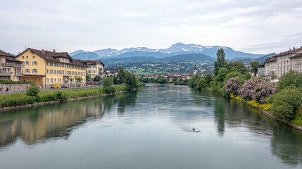 Fototapeta premium Serene River View with Alpine Mountains and Buildings