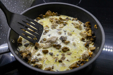 stirring creamy mushrooms and chicken in frying pan with black spatula