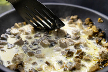 mushrooms and chicken in creamy sauce cooking in pan with spatula