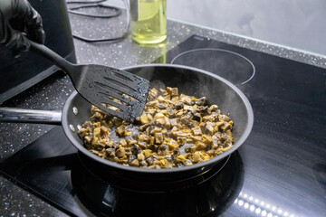 stirring sautéed mushrooms and chicken in a skillet on a stovetop with a black spatula