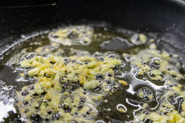 sizzling garlic frying in hot oil with bubbling texture on a nonstick pan, close-up of aromatic cooking process, golden garlic pieces floating in oil