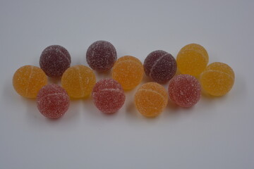 Original jelly Finnish candies in the form of round balls covered with white sugar. Yellow, orange, cherry, red gummy candies are located on a white plastic background.