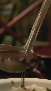 Closeup vertical slow motion footage of pouring feijoada on a plate of rice and steamed spinach