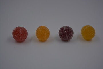 Original jelly Finnish candies in the form of round balls covered with white sugar. Yellow, orange, cherry, red gummy candies are located on a white plastic background.