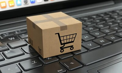 A small cardboard box with a shopping cart icon sits on a laptop keyboard, symbolizing online shopping. - Powered by Adobe