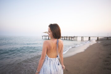 Woman Enjoying Peaceful Beach Sunset in Summer Dress with Ocean and Pier View