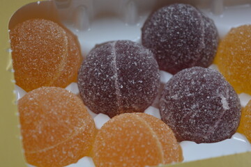 Original jelly Finnish candies in the form of round balls covered with white sugar. Yellow, orange, cherry, red gummy candies are arranged in white plastic packaging.