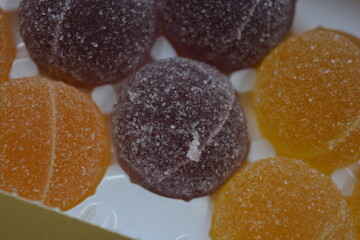 Original jelly Finnish candies in the form of round balls covered with white sugar. Yellow, orange, cherry, red gummy candies are arranged in white plastic packaging.