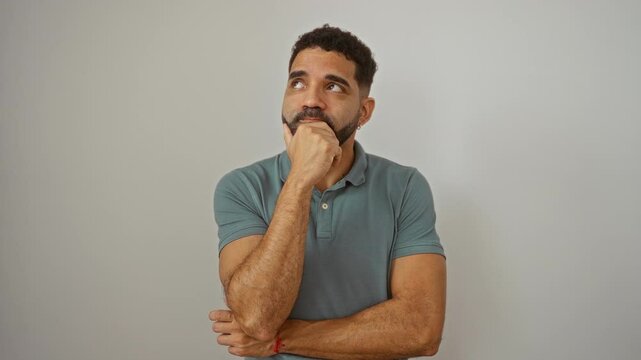 Young hispanic man standing and thinking with a serious face, hand on chin in thought about a confusing idea over isolated white background