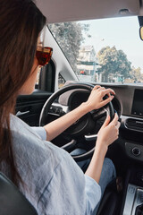 Naklejka premium Woman driving car, hands on steering wheel, eyes on phone screen, distracted driving