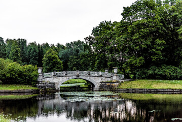 Small beautiful bridge over river in park, nice scenery on cloudy summer day