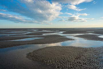 Sand at low tide with pools of water and ripples.