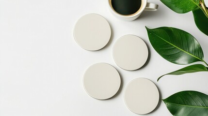 This image shows a minimalist coffee setup with a cup of coffee, four circular coasters, and lush green leaves on a clean white background.