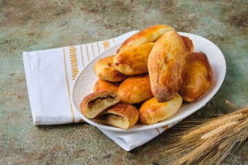 Pies with stewed fresh and pickled cabbage from yeast dough on a white ceramic dish on a green concrete background. Recipes cabbage.