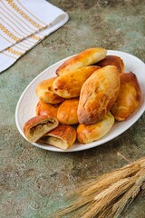 Pies with stewed fresh and pickled cabbage from yeast dough on a white ceramic dish on a green concrete background. Recipes cabbage.